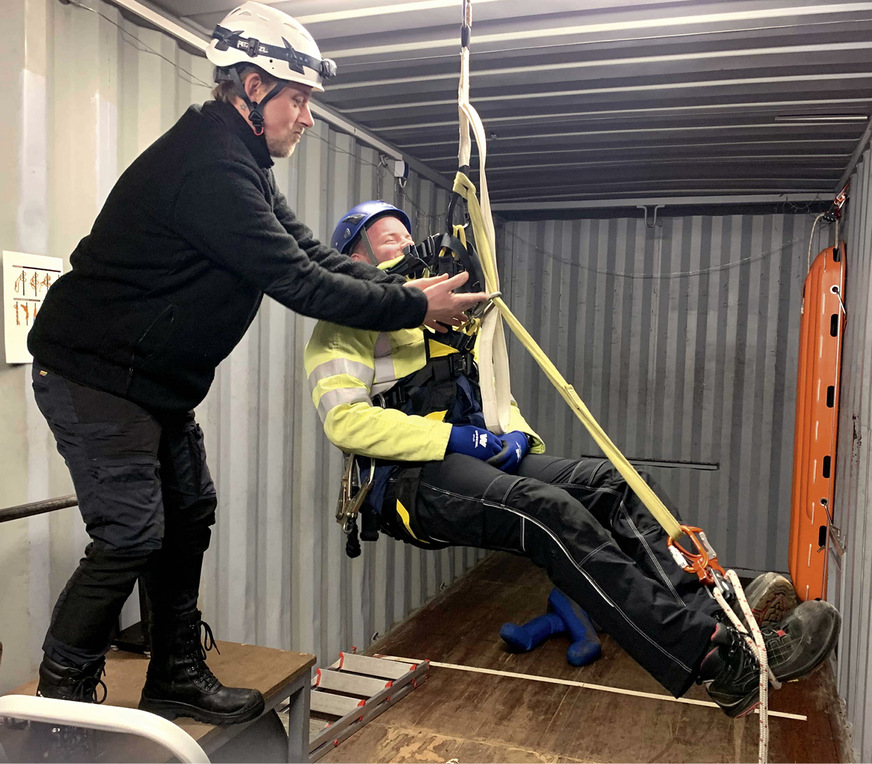 Lehrer Sven Sula hilft einem Schüler beim Aufbau einer Schlinge für die Füße zur Verhinderung des Hängetraumas und beim Einsatz des Rettungsgerätes.