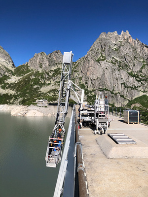 <p><strong>Solaranlagen an der Staumauer des Alpignasees</strong></p><p>Mit einem Brückenuntersichtgerät lassen sich die Handwerker auf die Montagehöhe herab.</p> - © Foto: EWZ