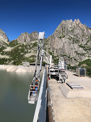 Solaranlagen an der Staumauer des AlpignaseesMit einem Brückenuntersichtgerät lassen sich die Handwerker auf die Montagehöhe herab.