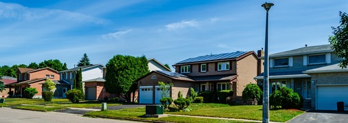 <p><strong>Energieautarkie - wann wird der Traum wahr?</strong></p><p>Panorama of a row of residential houses along a street, one with solar panels on the roof under a blue sky</p> - © Foto: G.R. Bender