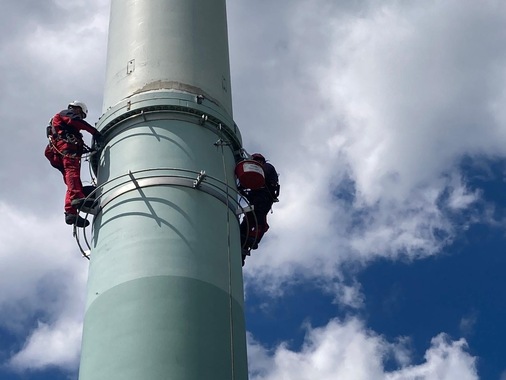 Zwei Arbeiter in Sicherheitsausrüstung besteigen einen hohen, hellblauen Industrieturm vor einem bewölkten Himmel. KTW Umweltschutztechnik GmbH