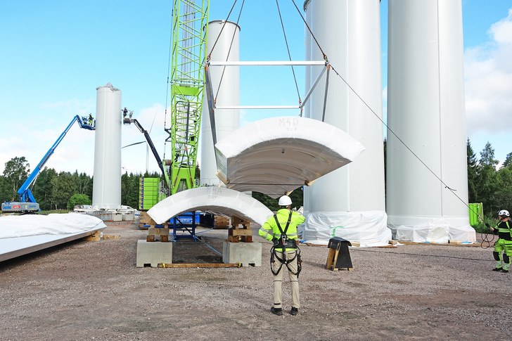 Ein herkömmlicher Kran kann die 14 Meter langen, hölzernen Viertelschalen für den Windkraft-Turm auf der Baustelle bewegen, da sie so leicht sind.