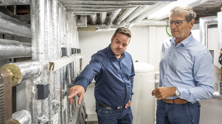 Zwei Männer in blauen Hemden untersuchen und besprechen isolierte Rohre und Steuerungen in einem Hauswirtschafts- oder Heizungskeller. - © Bundesverband Wärmepumpe