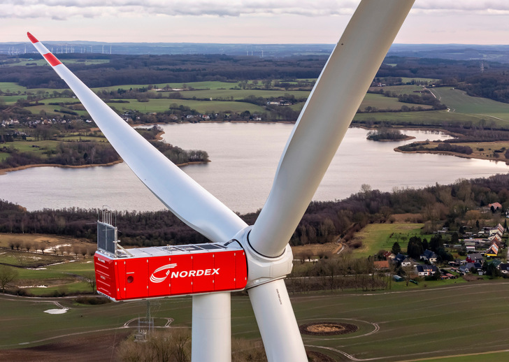 Nahaufnahme einer Nordex-Windkraftanlage mit einem See und einer ländlichen Landschaft im Hintergrund. - © Foto: Ulrich Mertens - Nordex