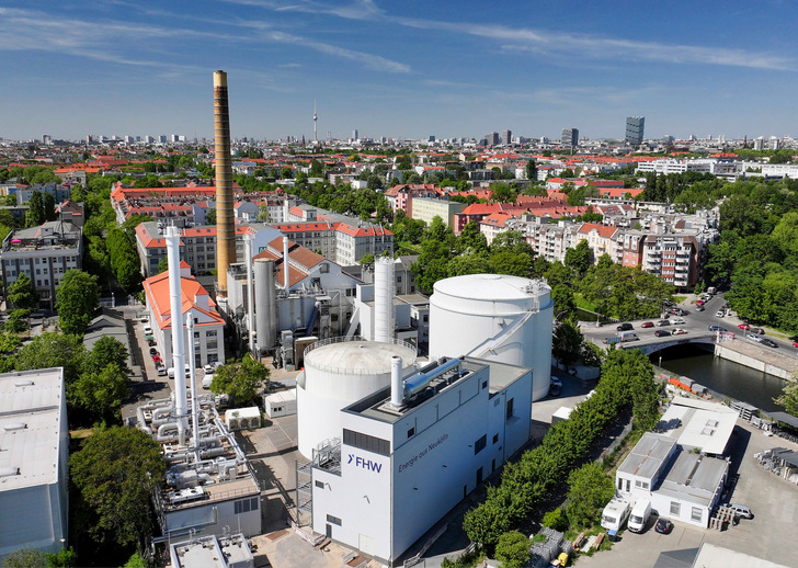 Luftaufnahme eines Kraftwerks mit weißen Gebäuden und Schornsteinen in einer Stadt mit roten Dächern und Grünanlagen. - © Andreas Friese - FHW Neukölln