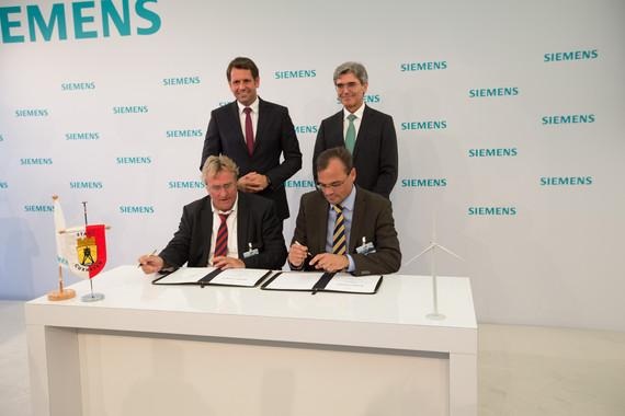 Siemens Cuxhaven | August 2015: Unterzeichnung der Ansiedlungsvereinbarung für eine Fertigung von Windenergieanlagen durch Siemens in Cuxhaven. Siemens-Windenergie-CEO Markus Tacke (sitzend rechts) und Cuxhavens Bürgermeister Ulrich Getsch signieren die Vereinbarung. Hinter ihnen repräsentieren der Siemens-Konzernchef Joe Kaeser (rechts) und Niedersachsens Wirtschaftsminister Olaf Lies (links) größere strategische Interessen.