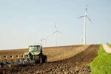 Traktor und Windenergieanlagen | Im ländlichen Raum spielt die Wertschöpfung durch Windenergie eine große Rolle. Kritiker der geplanten Ausschreibungen befürchten, dass Akteure wie Landwirte und Genossenschaften vom Markt verdrängt werden.