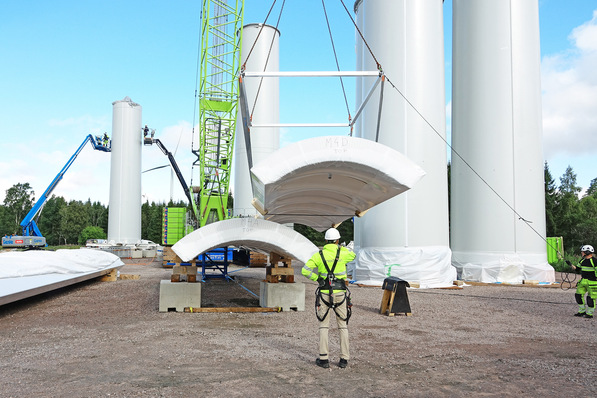 Ein herkömmlicher Kran kann die 14 Meter langen, hölzernen Viertelschalen für den Windkraft-Turm auf der Baustelle bewegen, da sie so leicht sind.