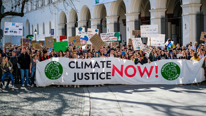 Eine große Gruppe von Menschen marschiert mit einem „Klimagerechtigkeit jetzt!“-Banner und hält verschiedene Protestschilder hoch. - © Fridays for Future