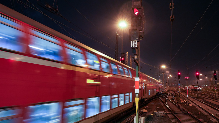 Ein roter Zug rast nachts unter hellem Licht vorbei, Gleise und Signallichter sind zu sehen. - © Deutsche Bahn AG / Volker Emersleben