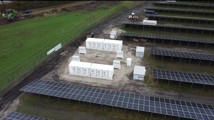 Luftaufnahme eines Solarparks mit Reihen von Solarmodulen und weißen Wirtschaftsgebäuden in der Mitte. - © Huawei