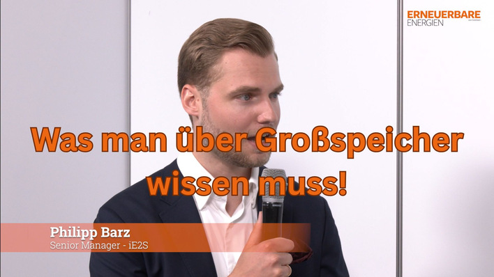 Ein Mann im Anzug spricht in ein Mikrofon; Der deutsche Text lautet: „Was man über Großspeicher wissen muss!“. - © GEM