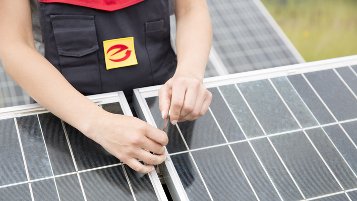 Person, die im Freien Solarmodule einstellt oder überprüft und eine Uniform mit einem gelb-roten Abzeichen trägt. - © ArGe Medien im ZVEH