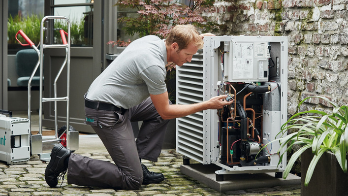 Ein Monteur baut eine Luft-Wasser-Wärmepumpe auf.