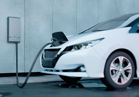 Ein weißes Elektroauto, das an einer an der Wand montierten Ladestation neben einer Betonwand geladen wird. - © Foto: Wallbox