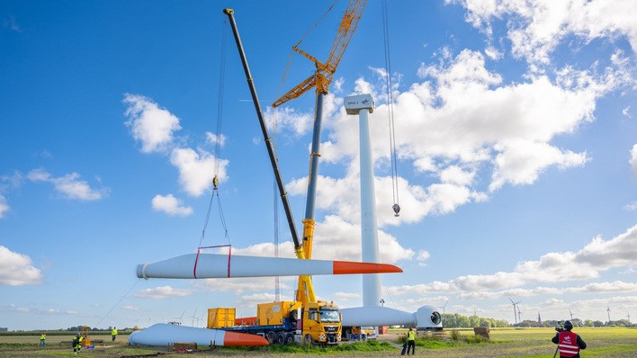 Ein Kran hob die jeweils 25 Meter langen und 2,5 Tonnen schweren Rotorblätter der OPUS 3 in Position, um sie noch am Boden an den Rotorstern der Anlage zu befestigen.